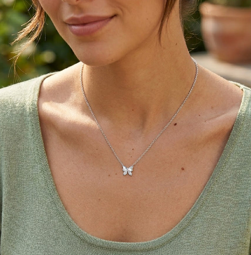 Close-up of a woman wearing a butterfly necklace with a blurred natural background