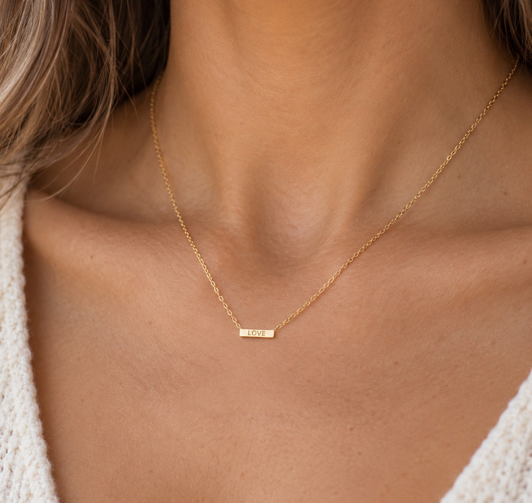 Gold love bar pendant necklace worn by female model