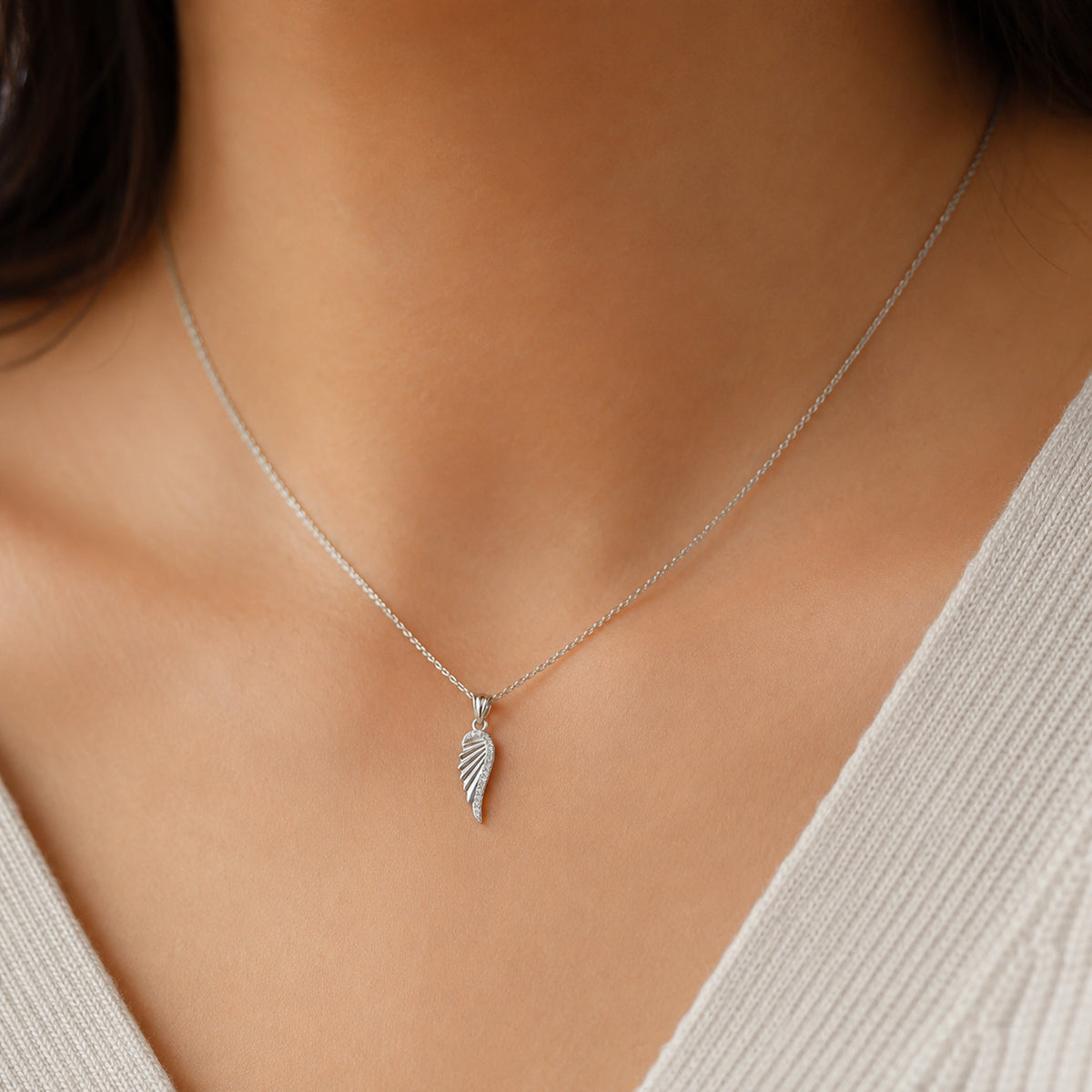 Silver necklace with a feather pendant on a person wearing a light-colored top.