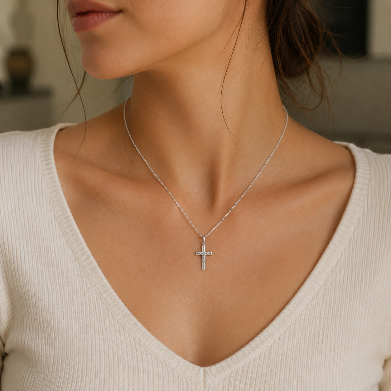 Silver cross necklace on a person wearing a white top