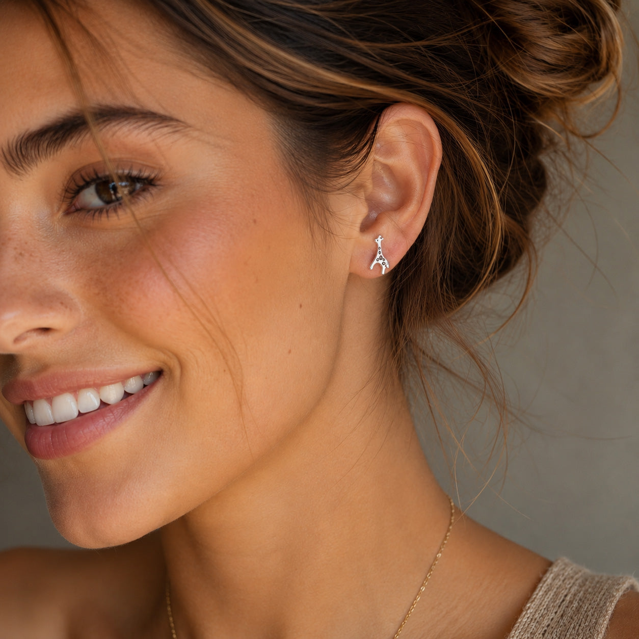 A close-up lifestyle shot of a woman wearing a small silver Eiffel Tower stud earring, with her hair in a bun and a neutral gray background.