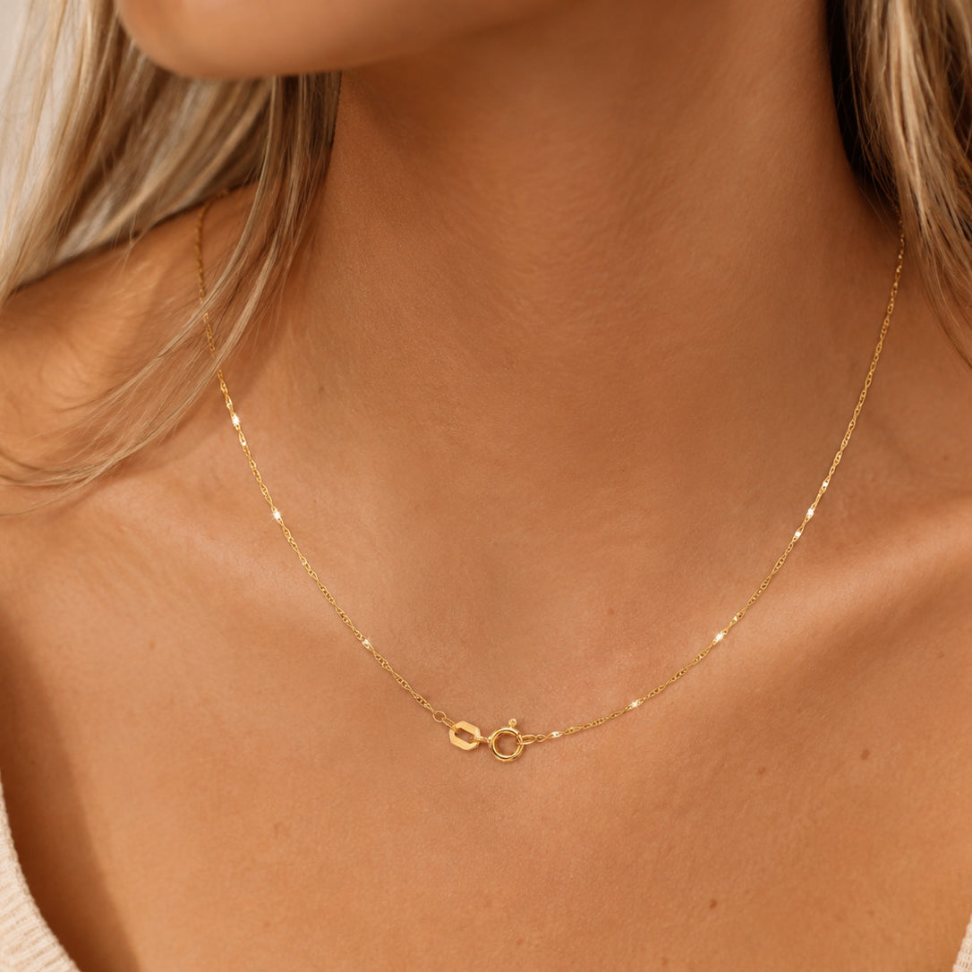 Close-up of a gold necklace on a person wearing a beige top.