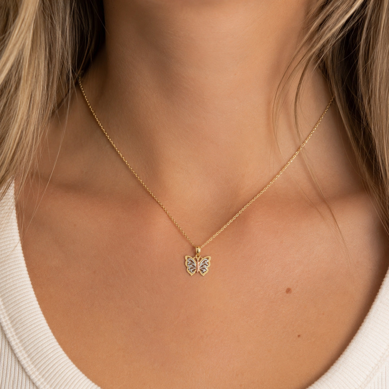 A delicate gold chain necklace with a small butterfly pendant, shown worn on a model's neck.