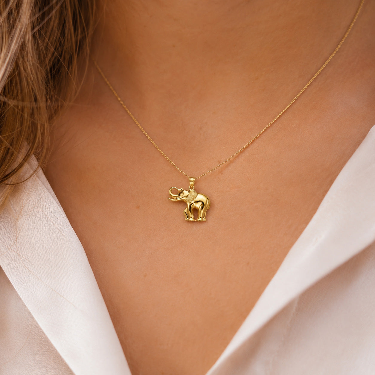 Gold elephant pendant necklace on a person wearing a white shirt.