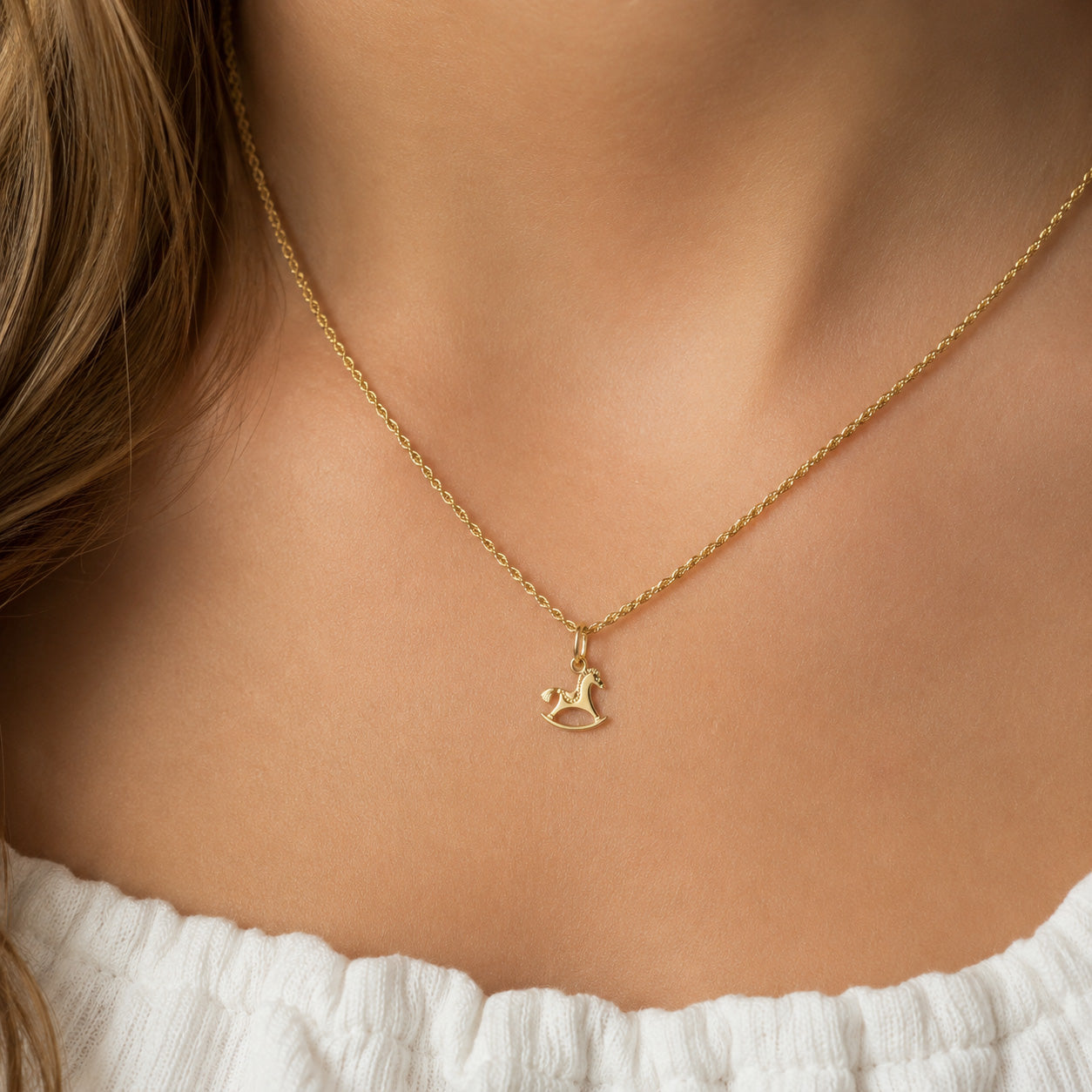 A delicate gold chain necklace with a small horse-shaped pendant, worn by a model in a close-up shot.