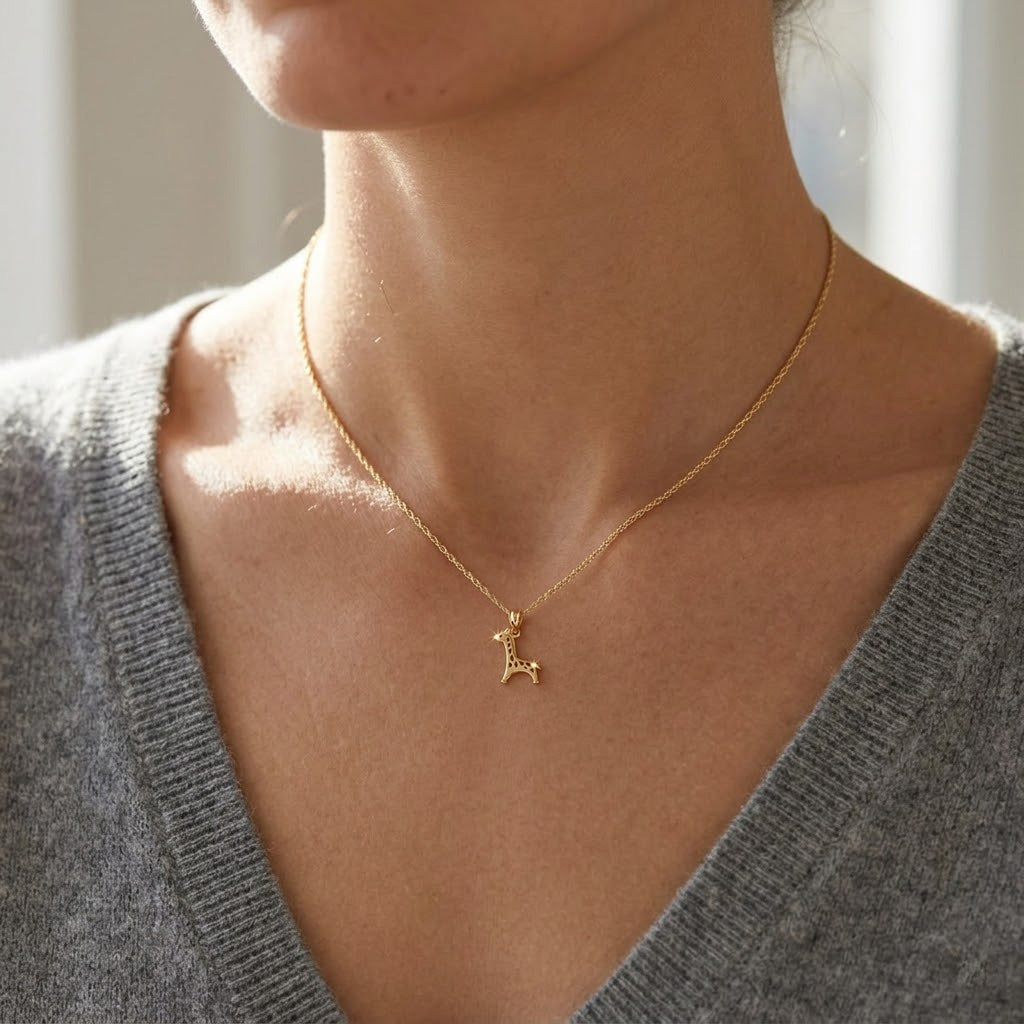 Gold necklace with a deer pendant worn by a person in a gray sweater.