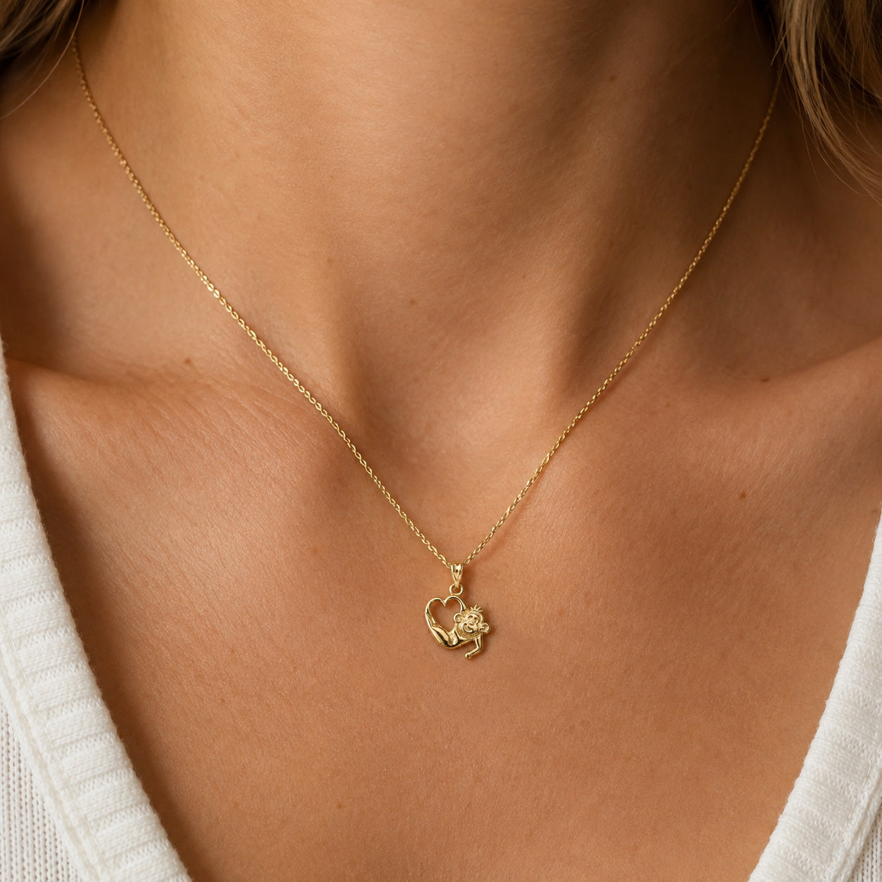 A close-up of a delicate gold chain necklace worn by a model, featuring a small heart-shaped pendant with a floral design, paired with a white ribbed top.