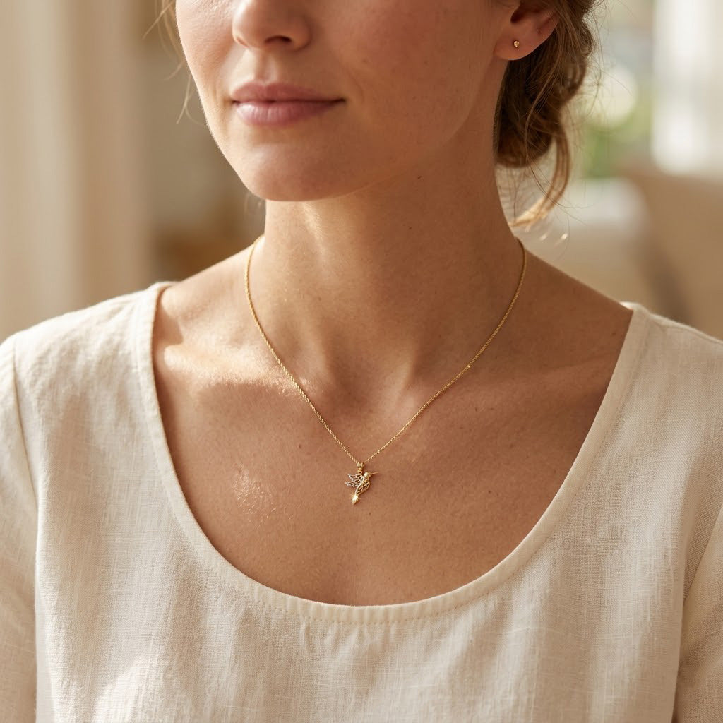 Woman wearing a delicate hummingbird gold necklace with a small pendant against a blurred background