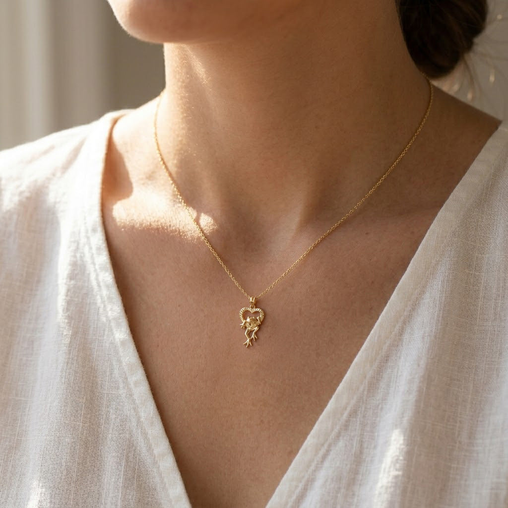 Gold necklace with a heart-shaped pendant worn by a person in a white top.