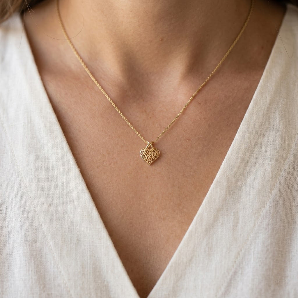 A delicate gold chain necklace with a small textured heart-shaped pendant, worn on a model's neck over a white V-neck top.