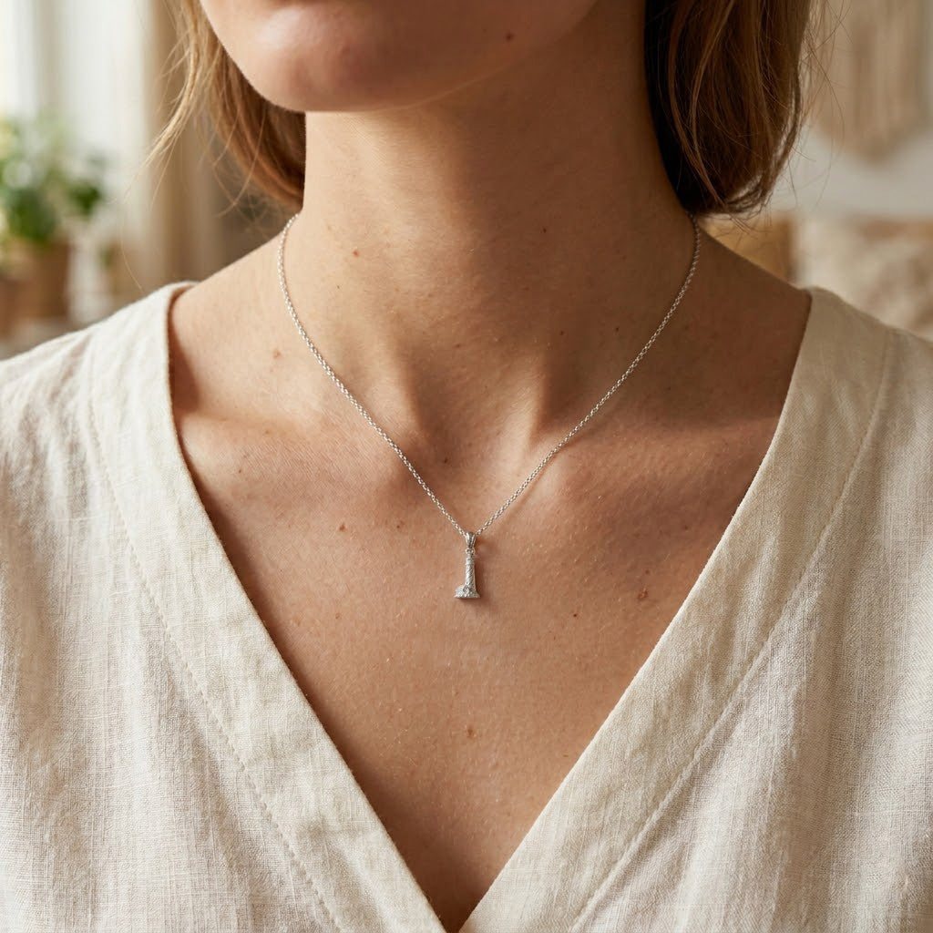 Close-up of a person wearing a silver necklace with a pendant indoors.