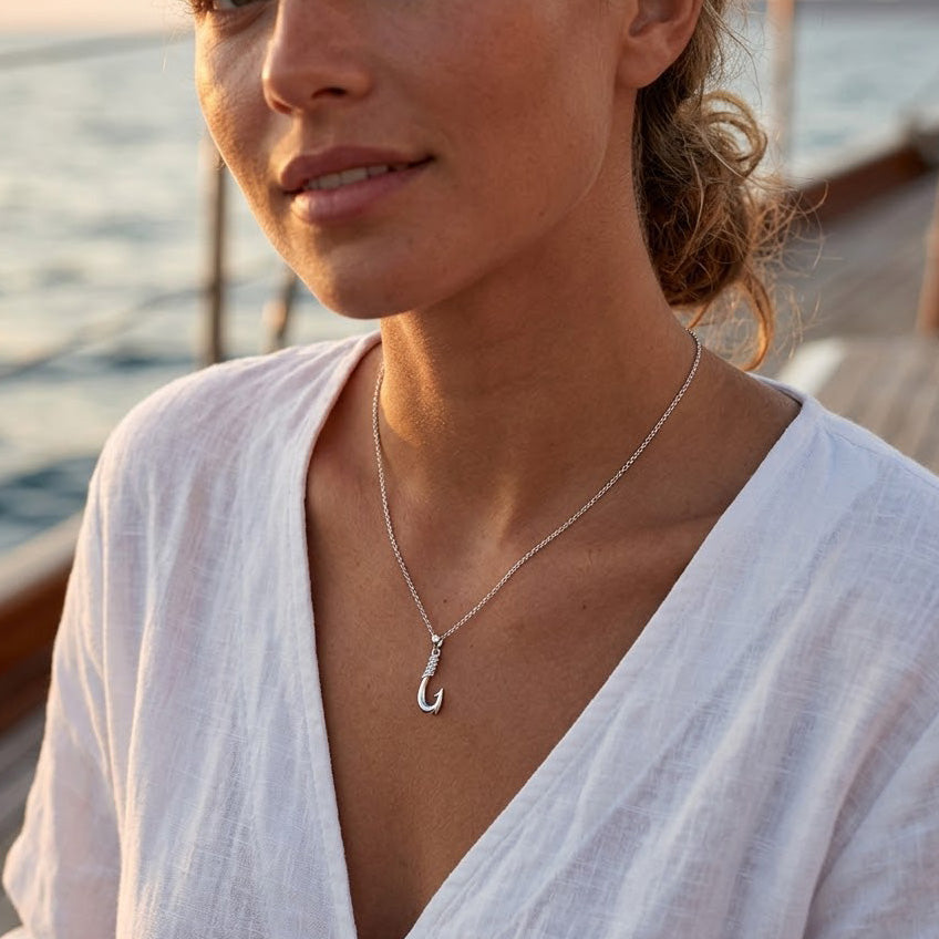 Woman wearing a silver necklace with a 'C' pendant by a body of water.