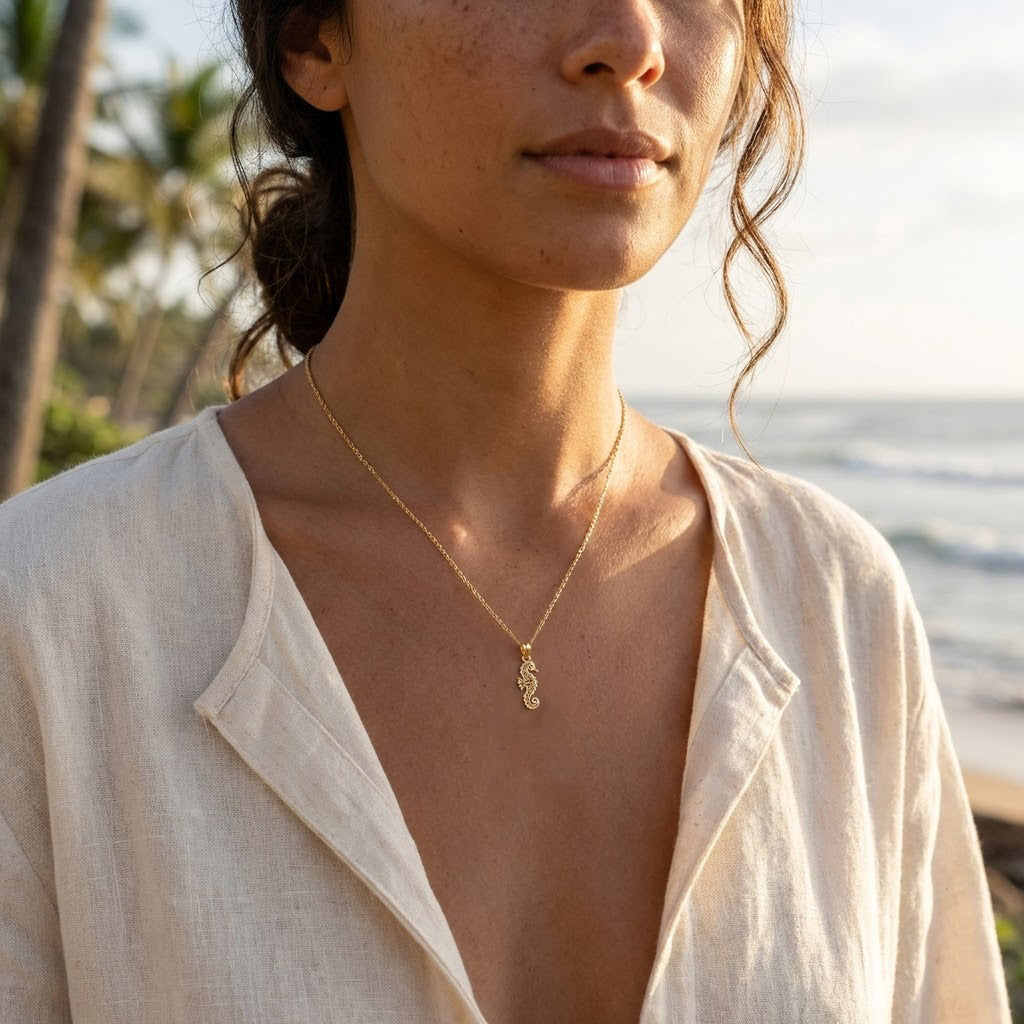 Woman wearing a gold necklace with a seahorse pendant against a blurred beach background