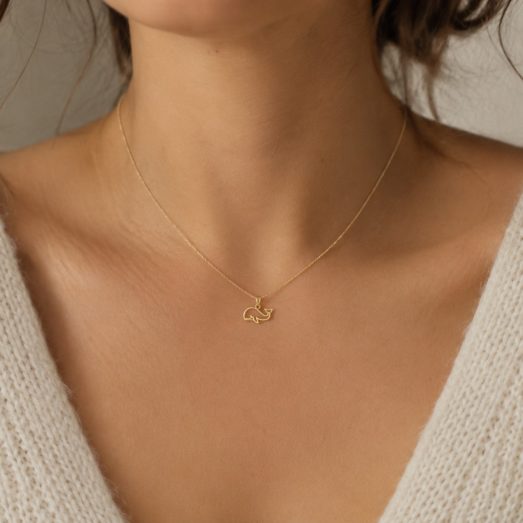 Gold necklace with a small pendant on a person wearing a beige sweater.