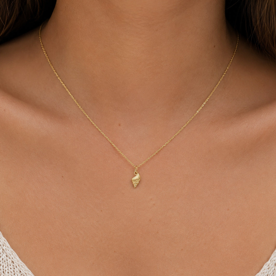 A delicate gold chain necklace with a small textured gold pendant, shown worn on a model's neck.