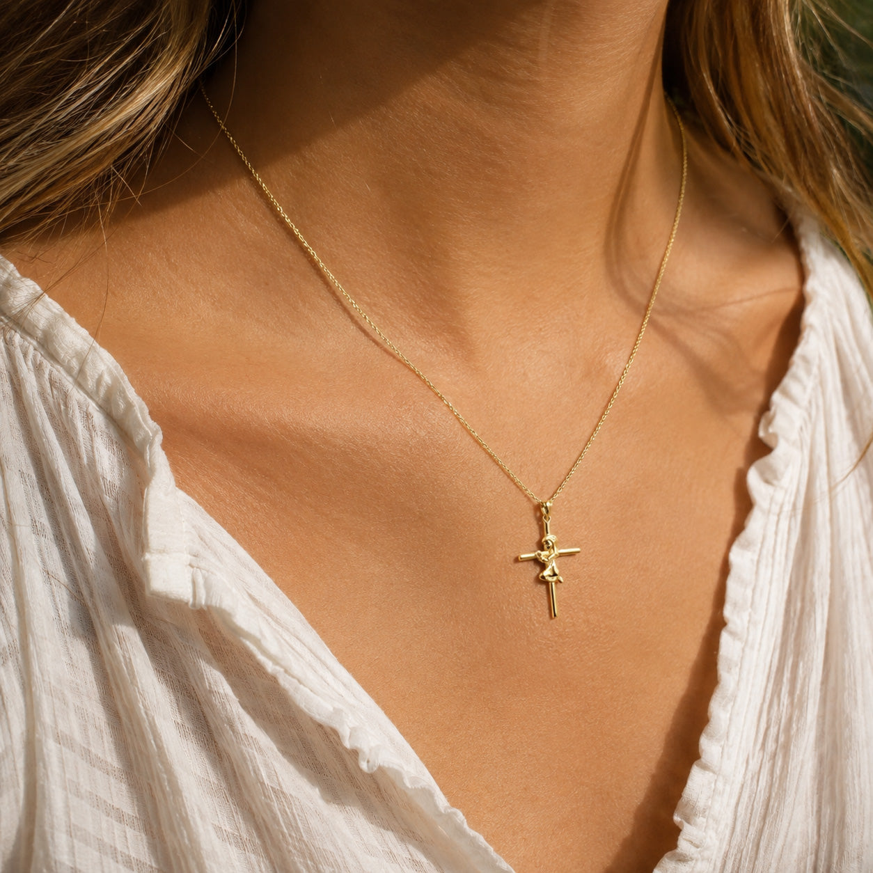 A delicate gold chain necklace with a small cross pendant worn by a model in warm natural light.
