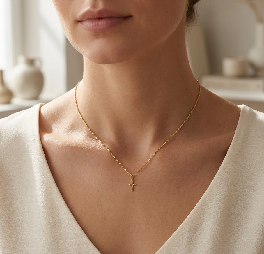 Gold necklace with a cross pendant on a person wearing a white top, blurred indoor background