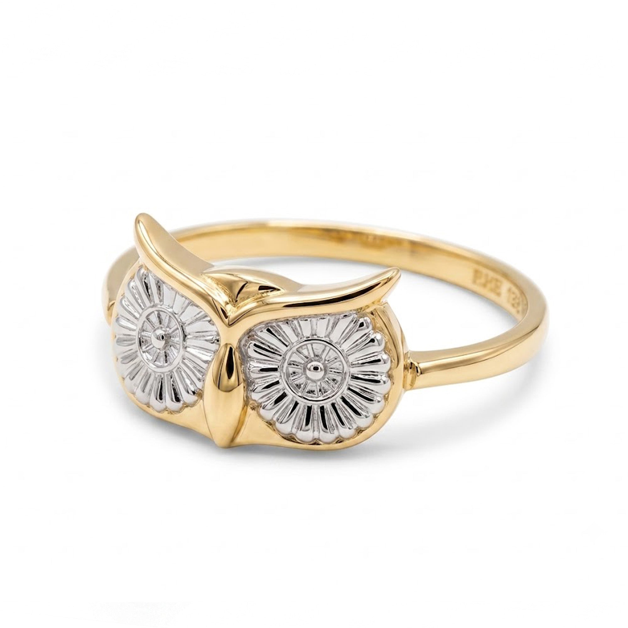 A gold owl ring featuring two circular owl eyes with textured silver-toned patterns and small clear stones, set on a polished gold band against a white background.