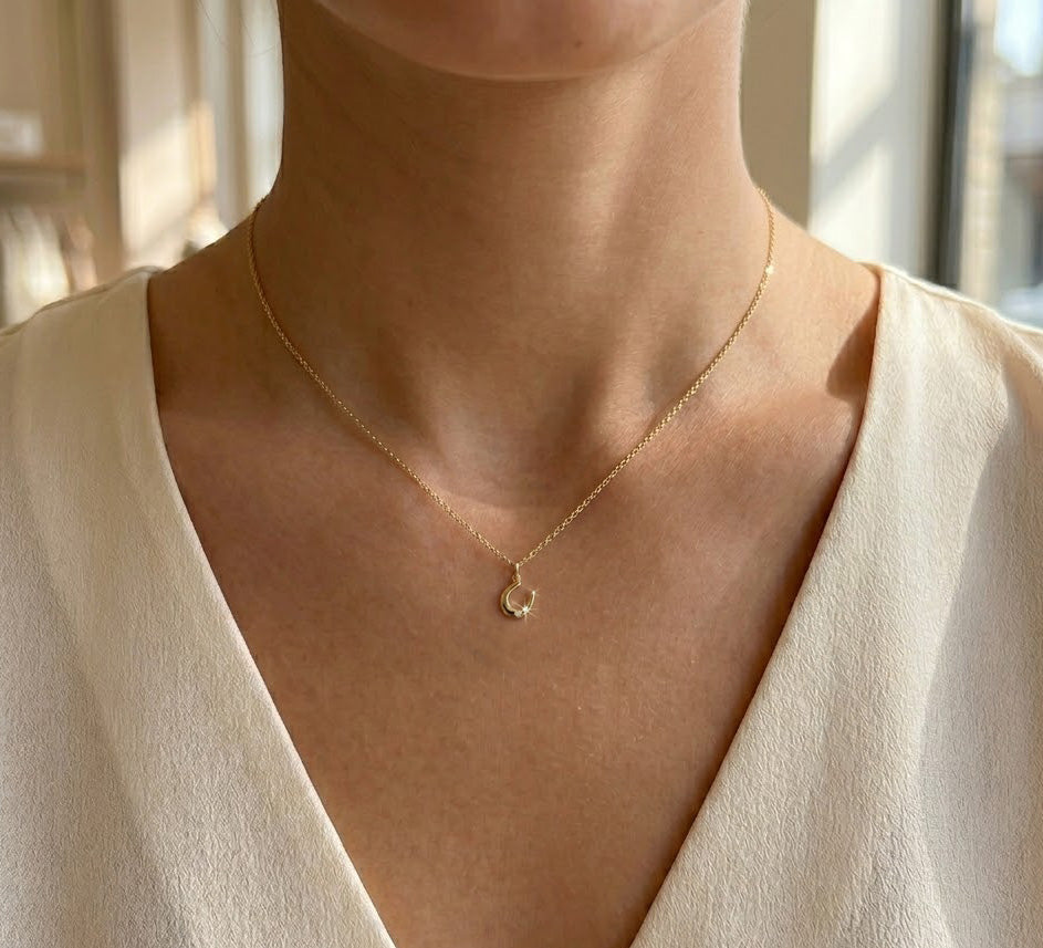 Gold necklace with a small pendant worn by a person in a light-colored top.
