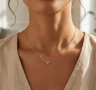 Gold necklace with an eye-shaped pendant on a person wearing a beige top.