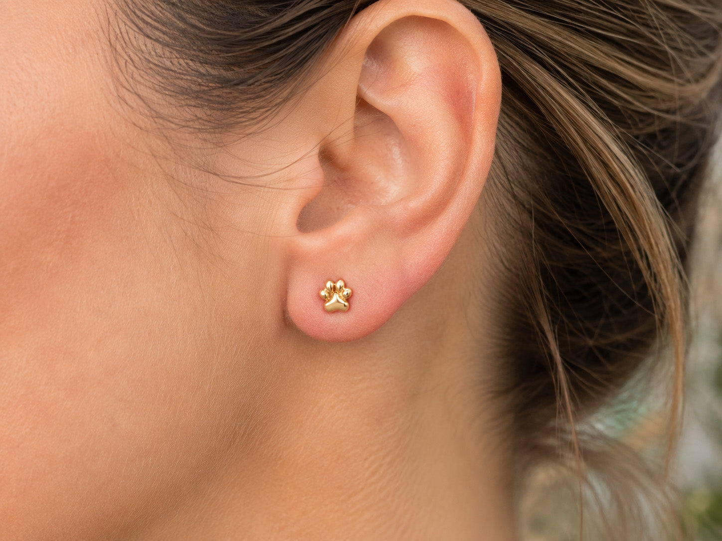 A close-up of a person's ear wearing a small gold stud earring shaped like a paw print.