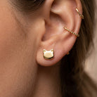Gold cat-shaped earring worn on an ear with a blurred background