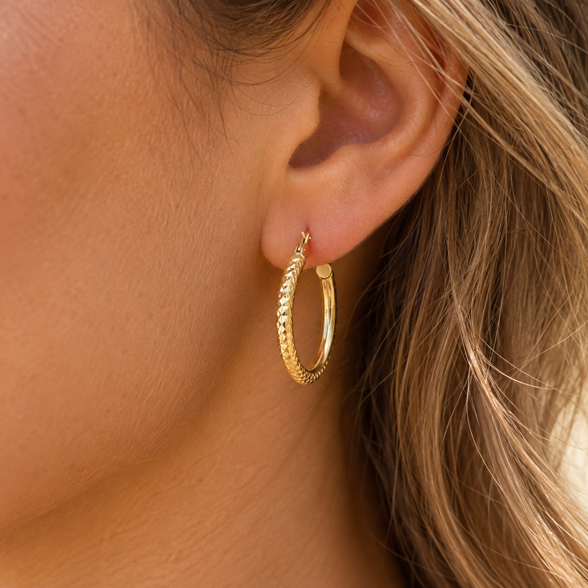 A close-up of a person's ear wearing a textured gold hoop earring.