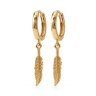 A pair of gold huggie hoop earrings with dangling feather charms, shown on a clean white background.