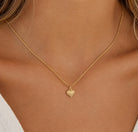 [group: small] A close-up of a model's neck and chest wearing a delicate gold chain necklace with a small textured heart-shaped pendant.