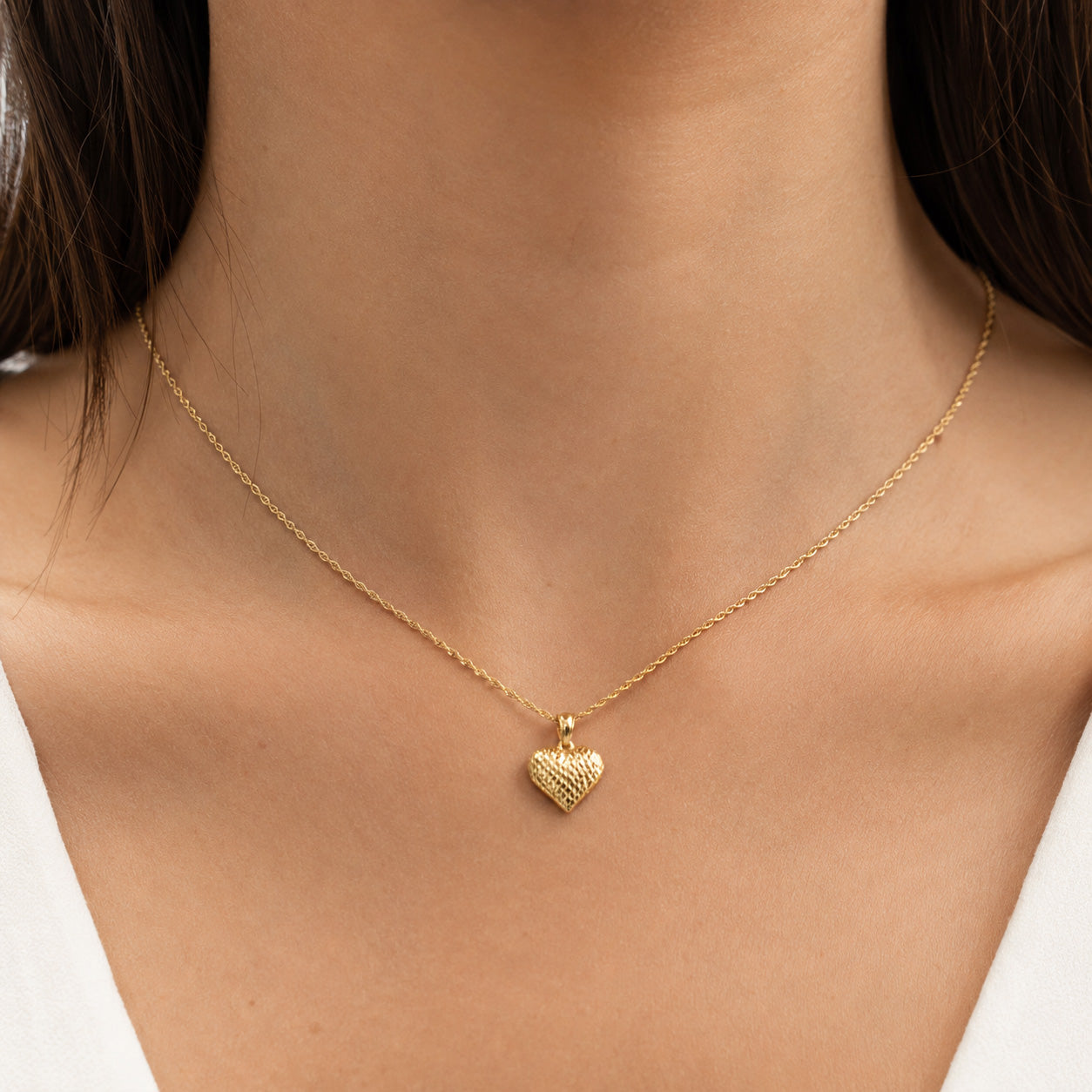 [group: medium] A delicate gold chain necklace with a small textured heart pendant, shown worn on a model's neck.
