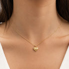 [group: medium] A delicate gold chain necklace with a small textured heart pendant, shown worn on a model's neck.