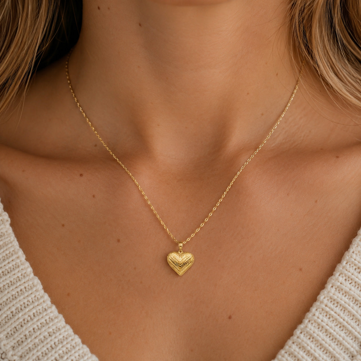 [group: large] A close-up of a model wearing a delicate gold chain necklace with a textured, ridged heart-shaped pendant.