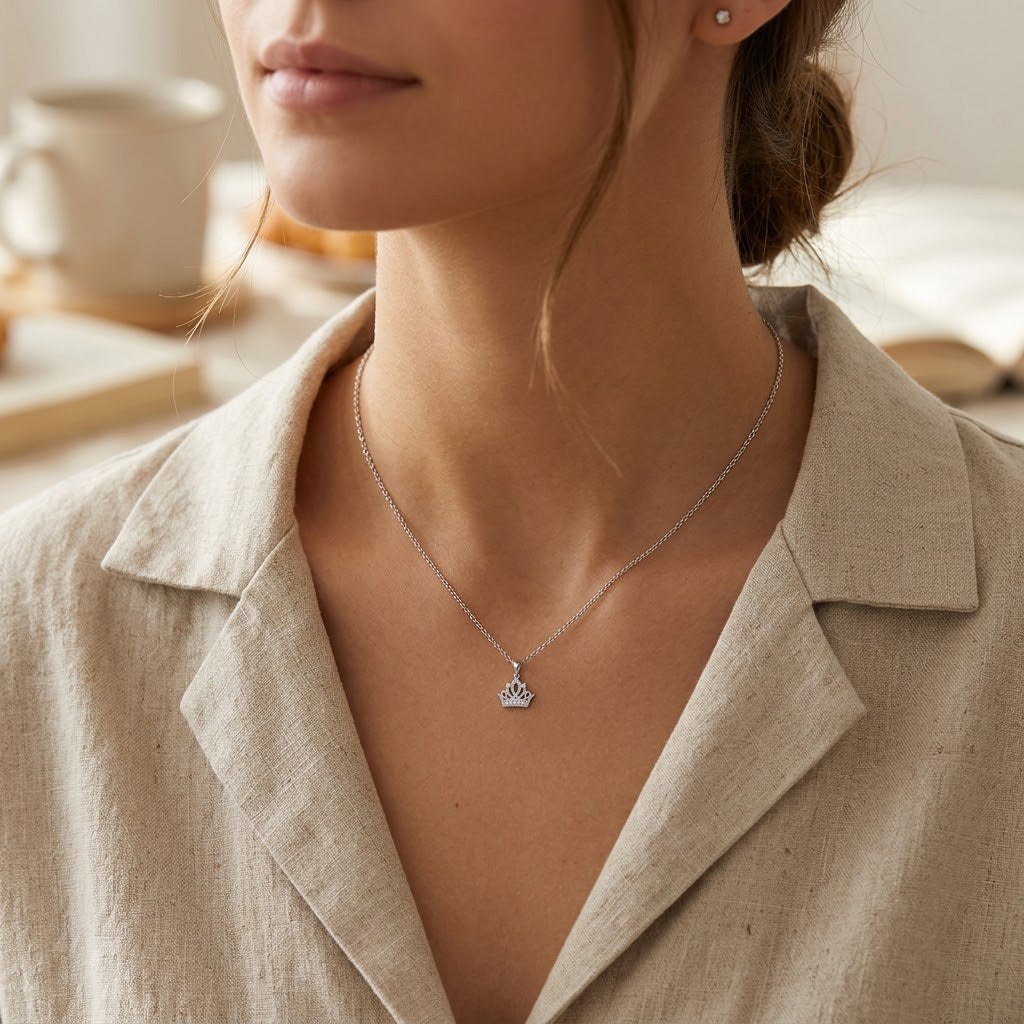 Close-up of a person wearing a silver necklace with a crown pendant, set against a neutral background.