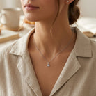 Close-up of a person wearing a silver necklace with a crown pendant, set against a neutral background.