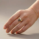 Hand wearing a gold ring with a black and yellow design on a neutral background