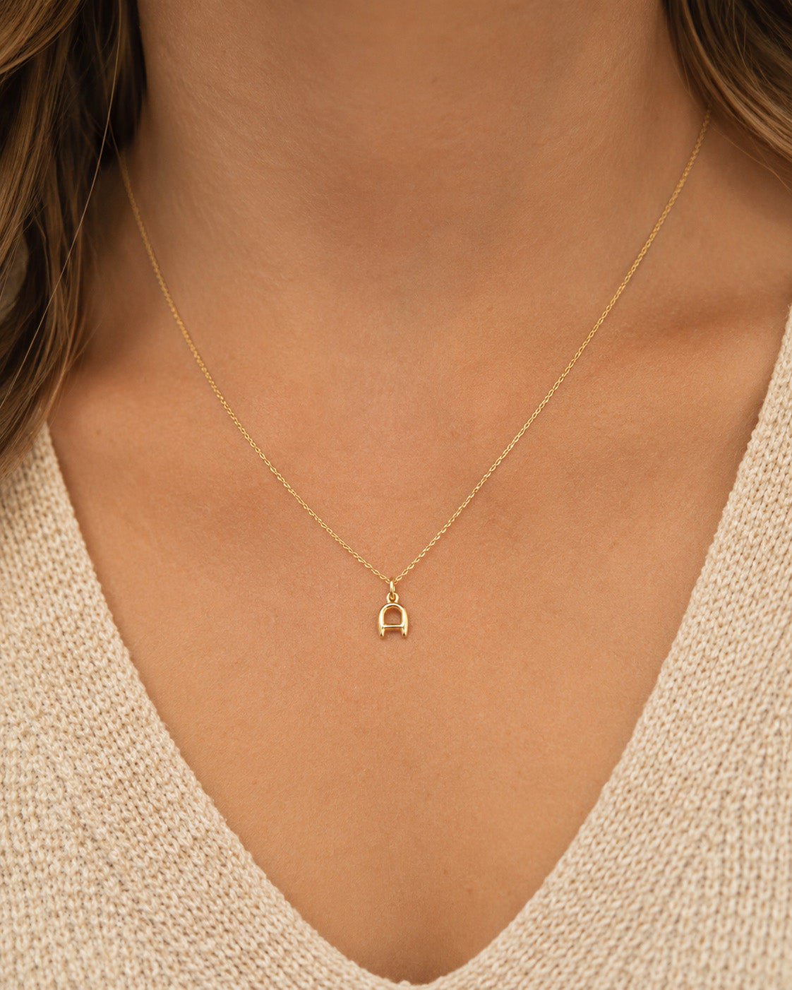[group: a-10k-gold]A delicate gold necklace with a small letter 'A' pendant, shown worn on a model's neck over a beige knit V-neck top.
