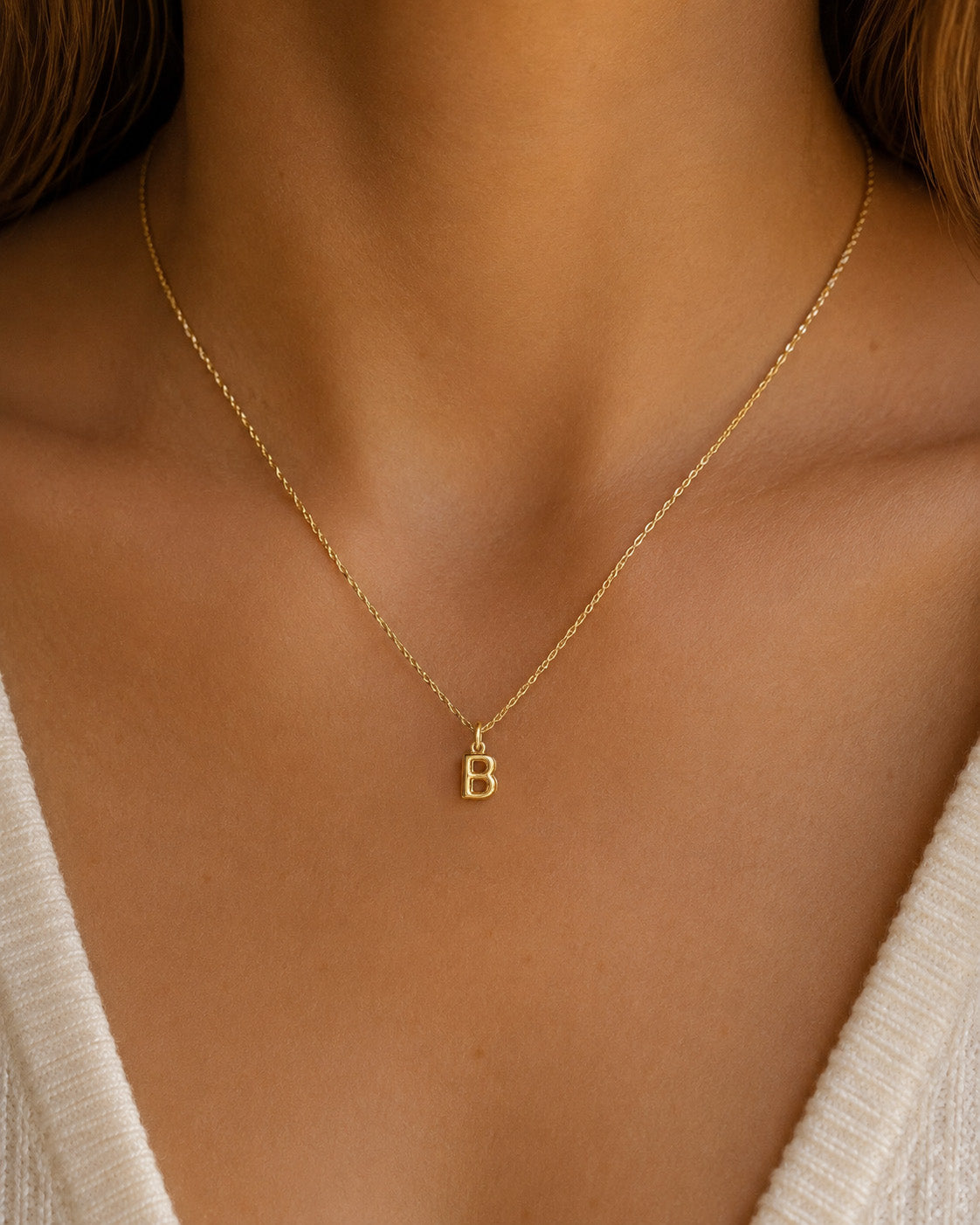 [group: b-10k-gold]A delicate gold chain necklace with a small letter 'B' initial pendant, shown worn on a model's neck.