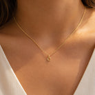 [group: c-10k-gold]A delicate gold chain necklace with a small crescent moon pendant, shown worn on a model's neck over a white V-neck top.