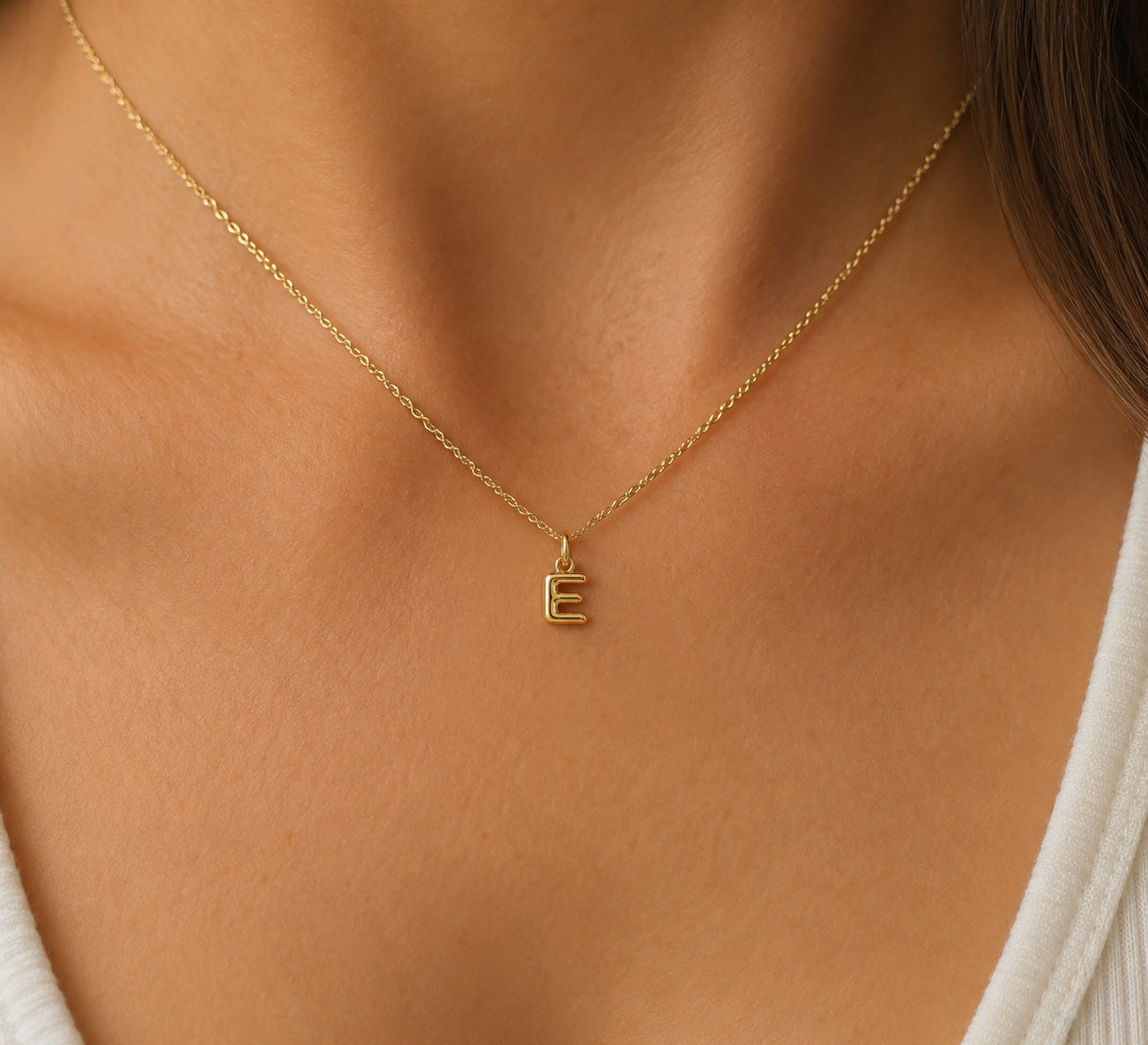 [group: e-10k-gold] A delicate gold chain necklace with a small capital letter 'E' pendant, shown worn on a model's neck.