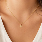 [group: g-10k-gold]A delicate gold chain necklace with a small lowercase letter 'c' initial pendant, shown worn on a model's neck over a white V-neck top.