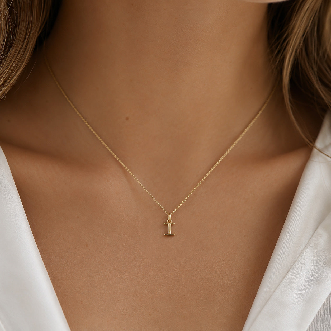 [group: i-10k-gold]A delicate gold chain necklace with a small initial pendant featuring the letter 'I' in a cross-style design, shown worn on a model's neck.