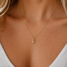[group: k-10k-gold]A close-up of a model's neck and chest wearing a delicate gold chain necklace with a small initial pendant spelling 'K'.