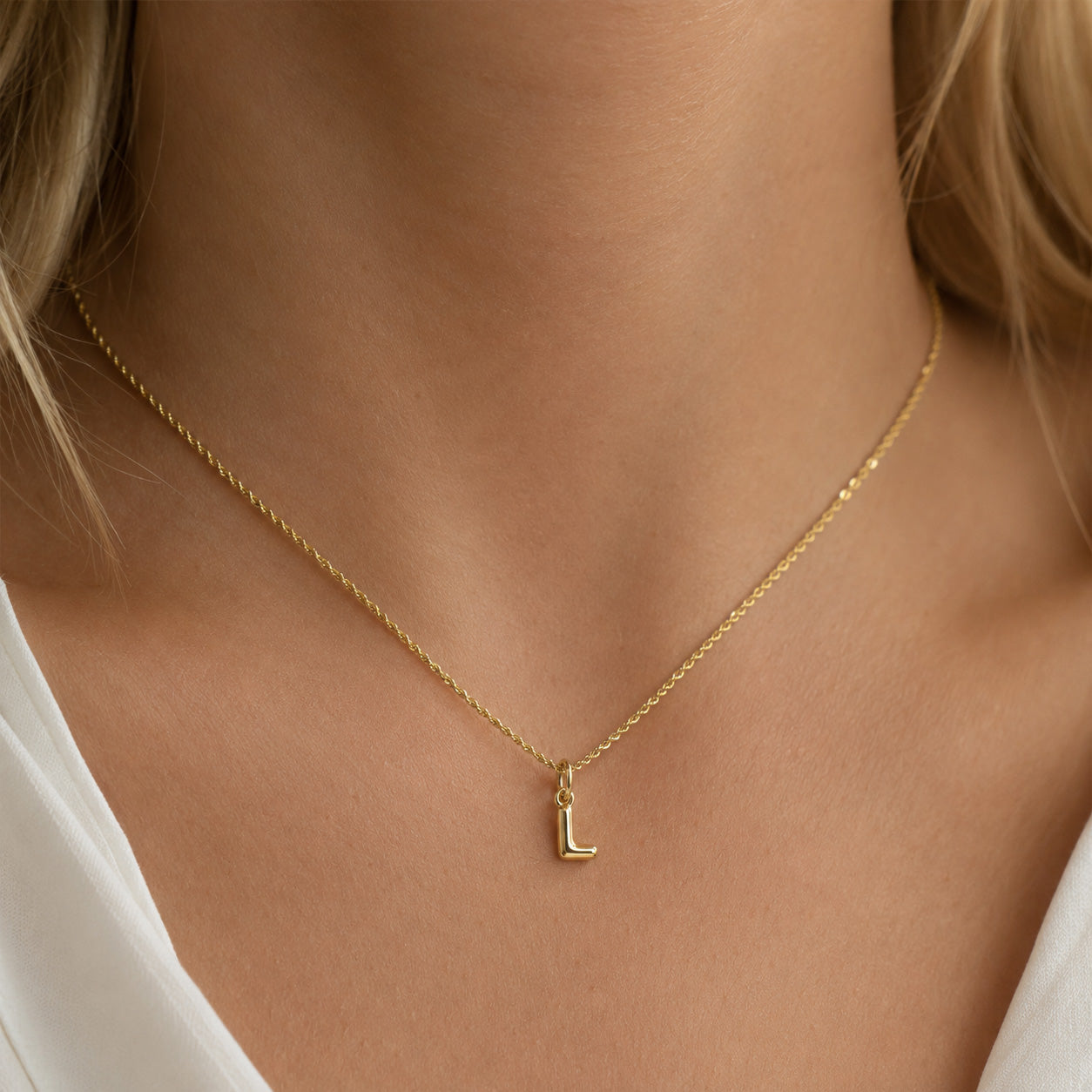 [group: l-10k-gold]A close-up of a model's neck and upper chest wearing a delicate gold chain necklace with a small letter 'L' pendant.