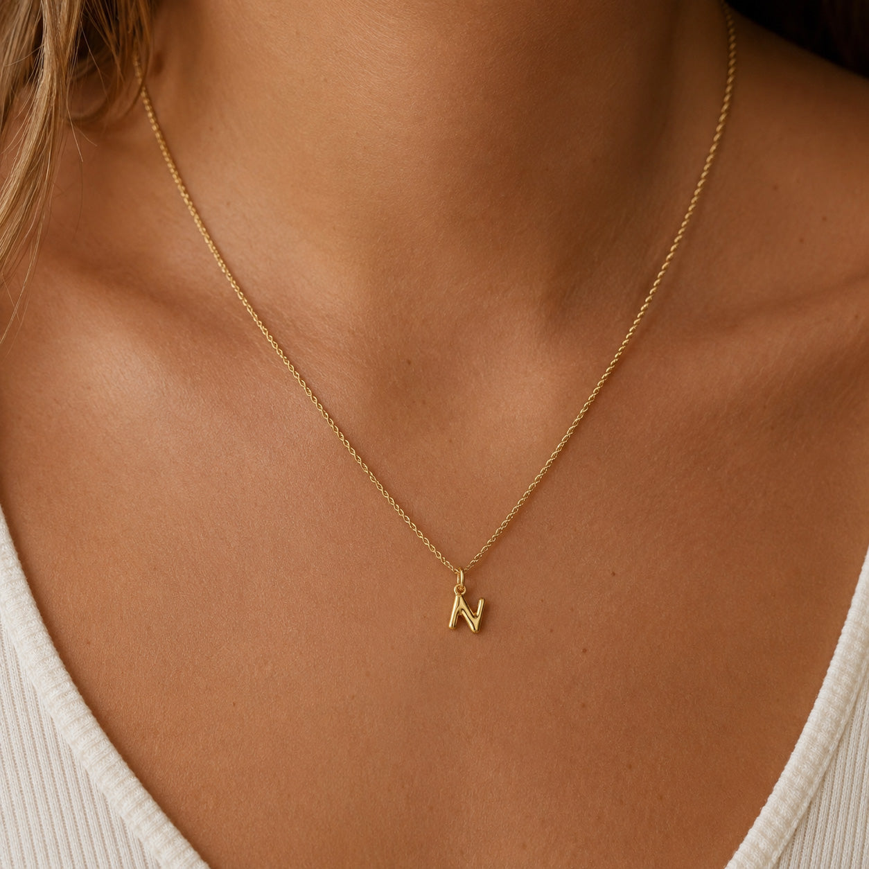 [group: n-10k-gold] A close-up of a delicate gold chain necklace worn by a model, featuring a small initial pendant engraved with the letter 'N'.