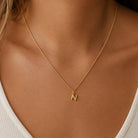 [group: n-10k-gold] A close-up of a delicate gold chain necklace worn by a model, featuring a small initial pendant engraved with the letter 'N'.
