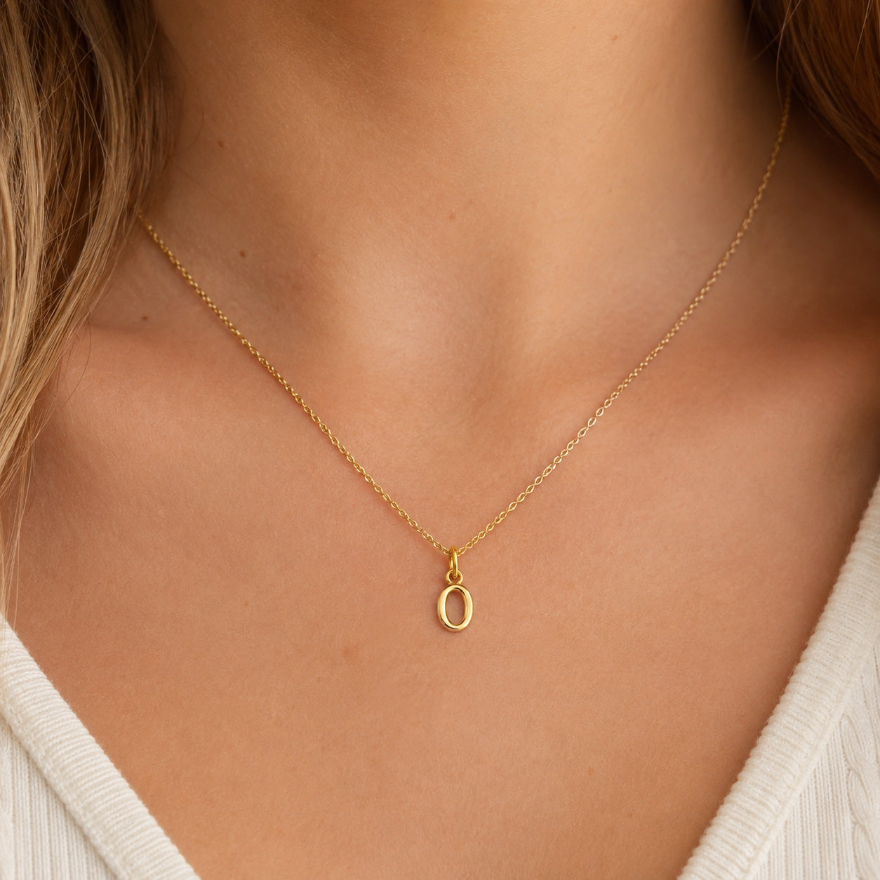 [group: o-10k-gold]A delicate gold chain necklace with a small oval pendant, worn on a model's neck over a white ribbed top.