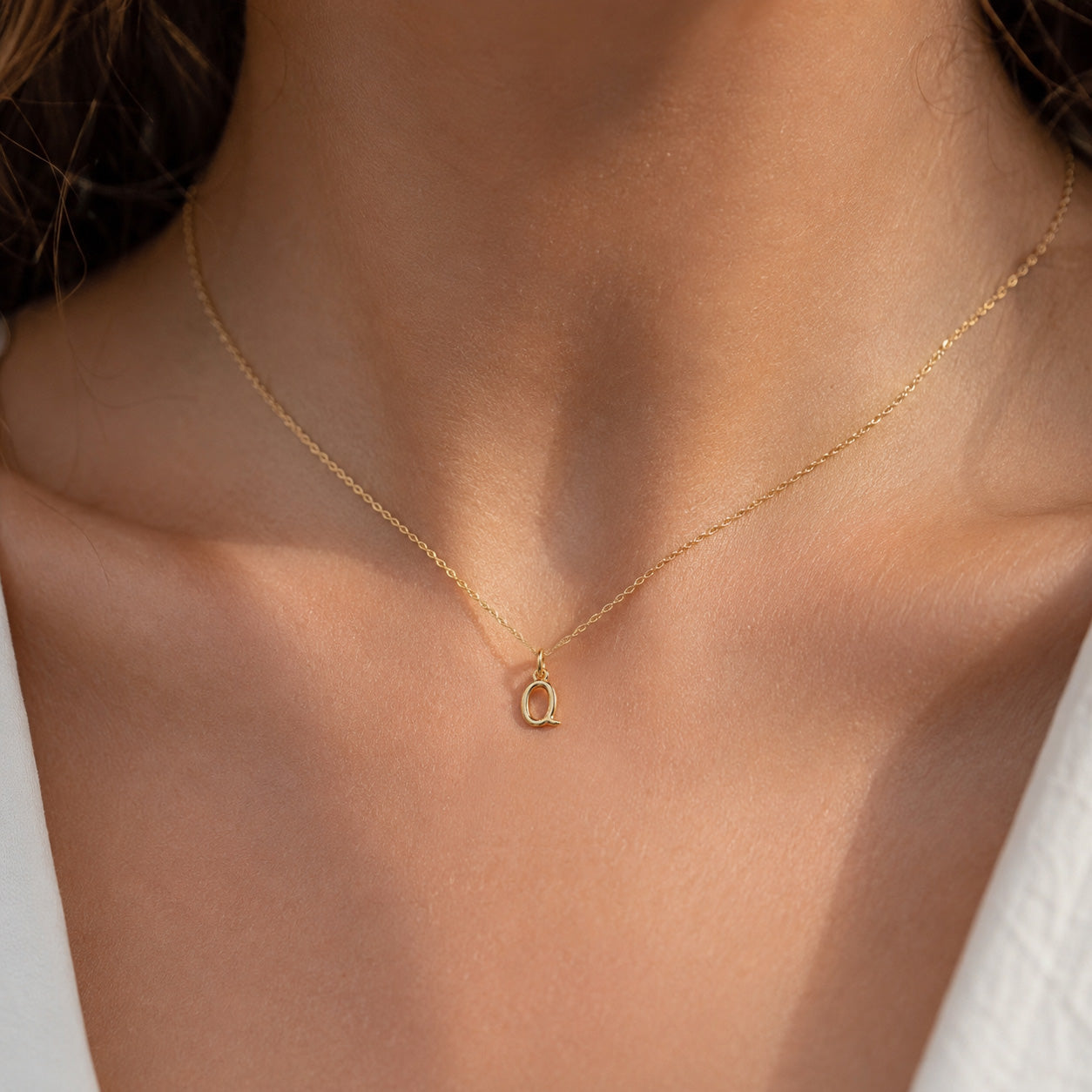 [group: q-10k-gold]A delicate gold chain necklace with a small letter 'Q' pendant, worn on a model's neck.