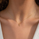 [group: q-10k-gold]A delicate gold chain necklace with a small letter 'Q' pendant, worn on a model's neck.