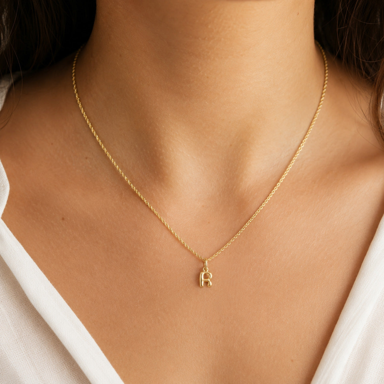 [group: r-10k-gold] A delicate gold chain necklace with a small letter 'R' initial pendant, shown worn on a model's neck.