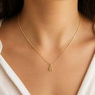 [group: r-10k-gold] A delicate gold chain necklace with a small letter 'R' initial pendant, shown worn on a model's neck.